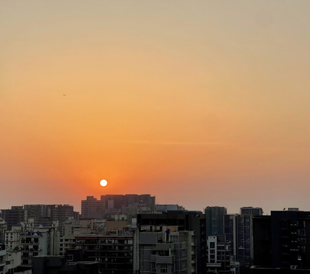 Mumbai's skyscrapers in the foreground, a spectacular sunset in the background. A plane is seen in the orange sky.